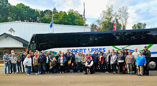 Group of passengers posing in front of a Great Lakes Motor Coach 56-passenger bus, showcasing group travel for tours and outings.