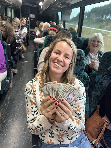 Smiling woman holding cash on a charter bus, surrounded by passengers, highlighting group travel experience with Great Lakes Motor Coach.